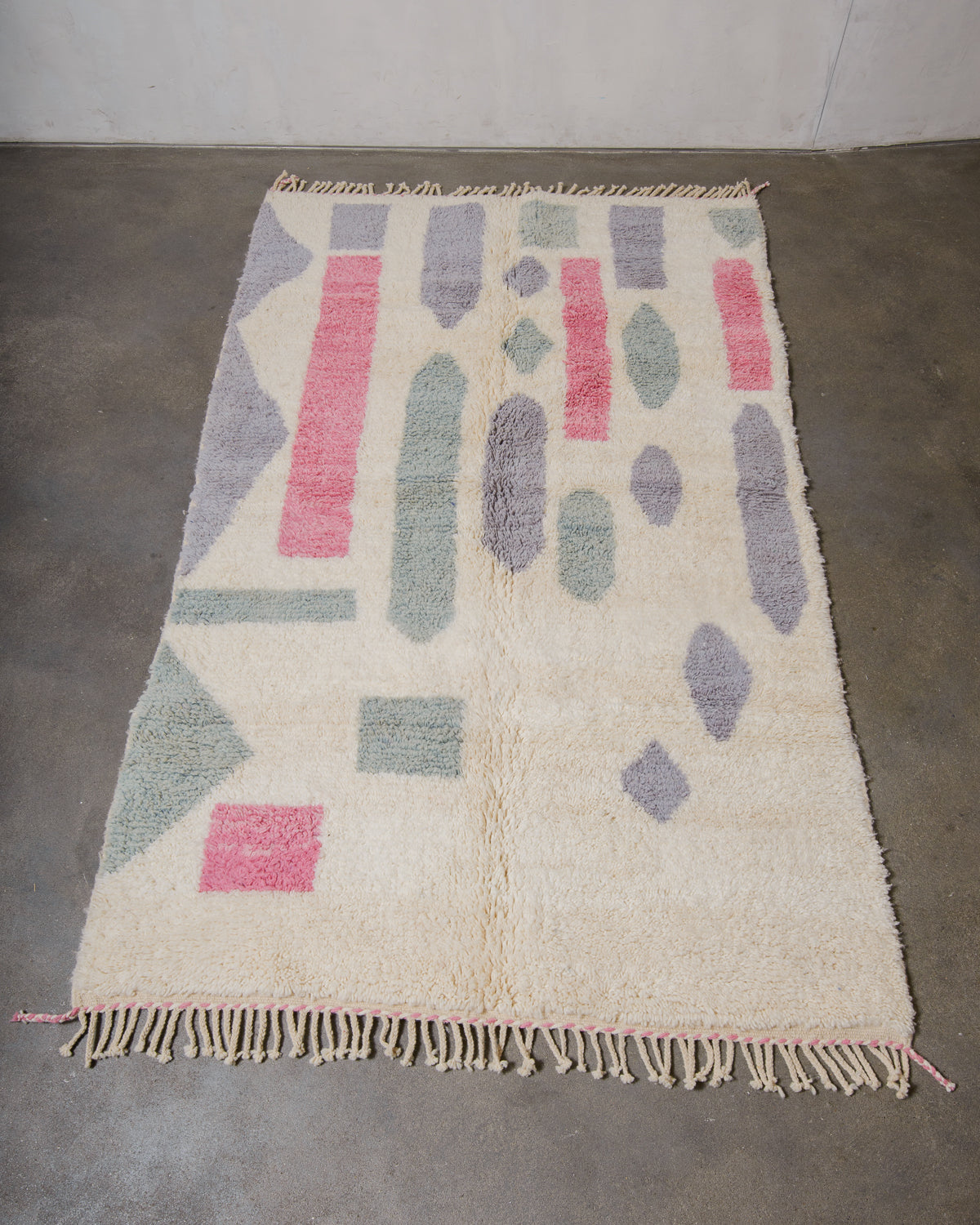 Beniourain rug in cream, pink, lavender and sage, laying on cement floor.
